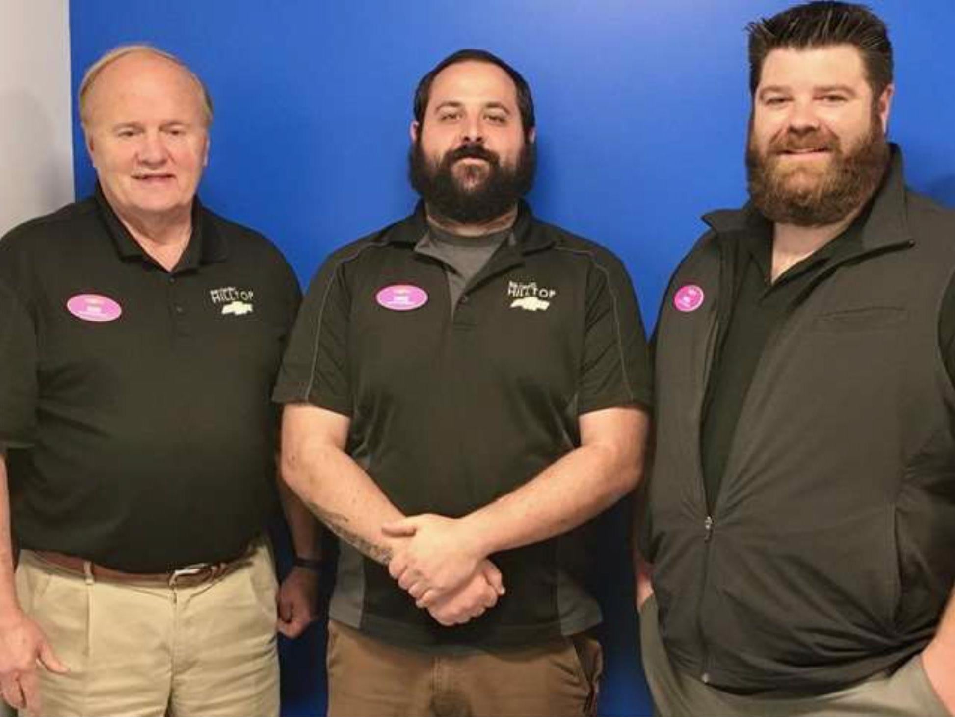 Three individuals stand side by side against a blue background, wearing black shirts