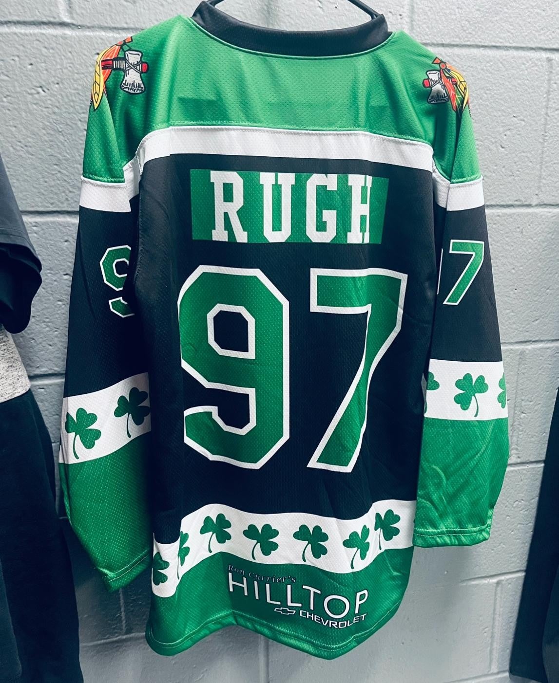 Green and black hockey jersey with the name RUGH and number 97 in white. Shamrock designs on sleeves and bottom. Logos on shoulders and advertisement for THE HILLTOP ICE ARENA at the bottom.