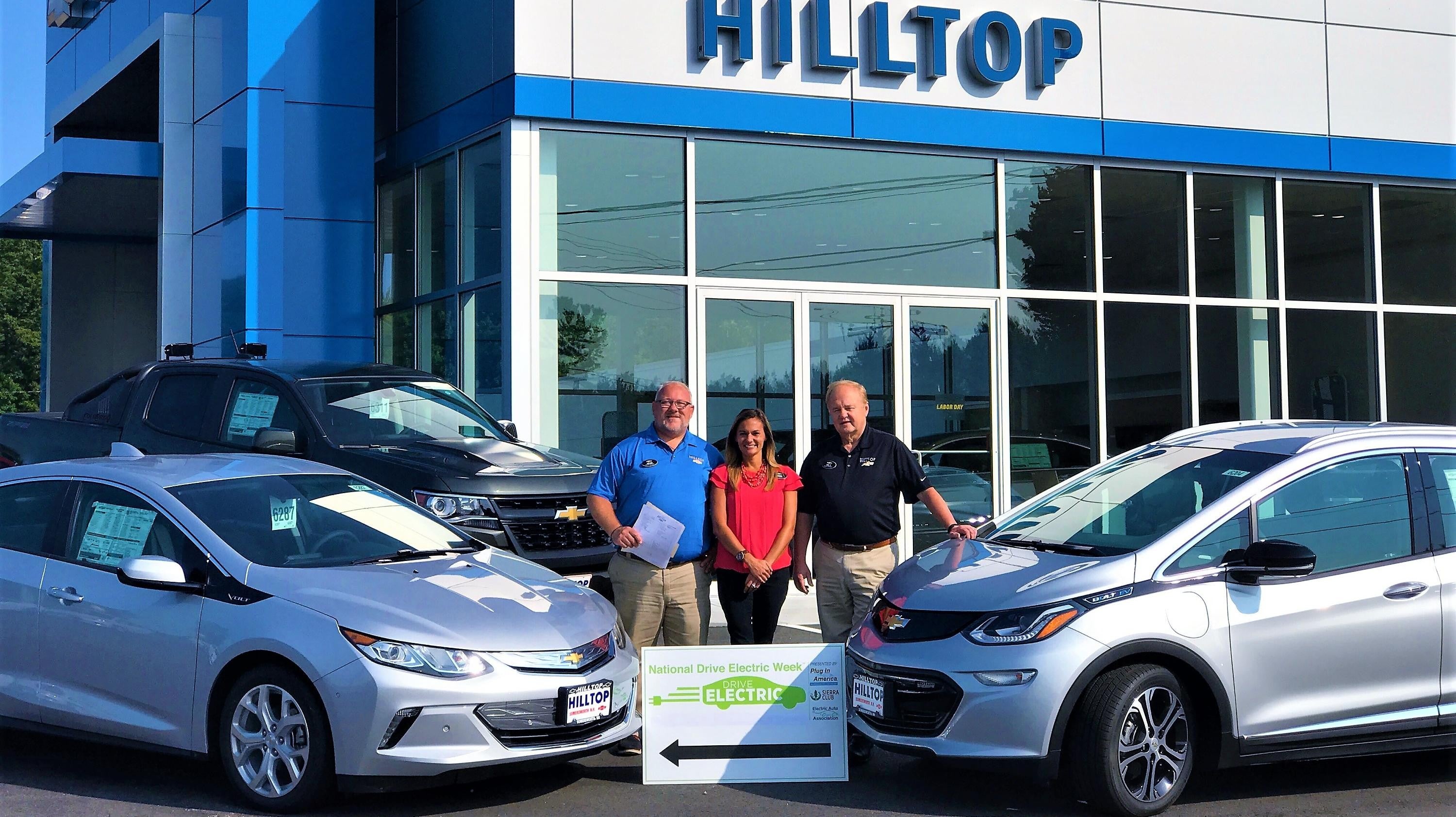 three people stand in front of a Hilltop car dealership.