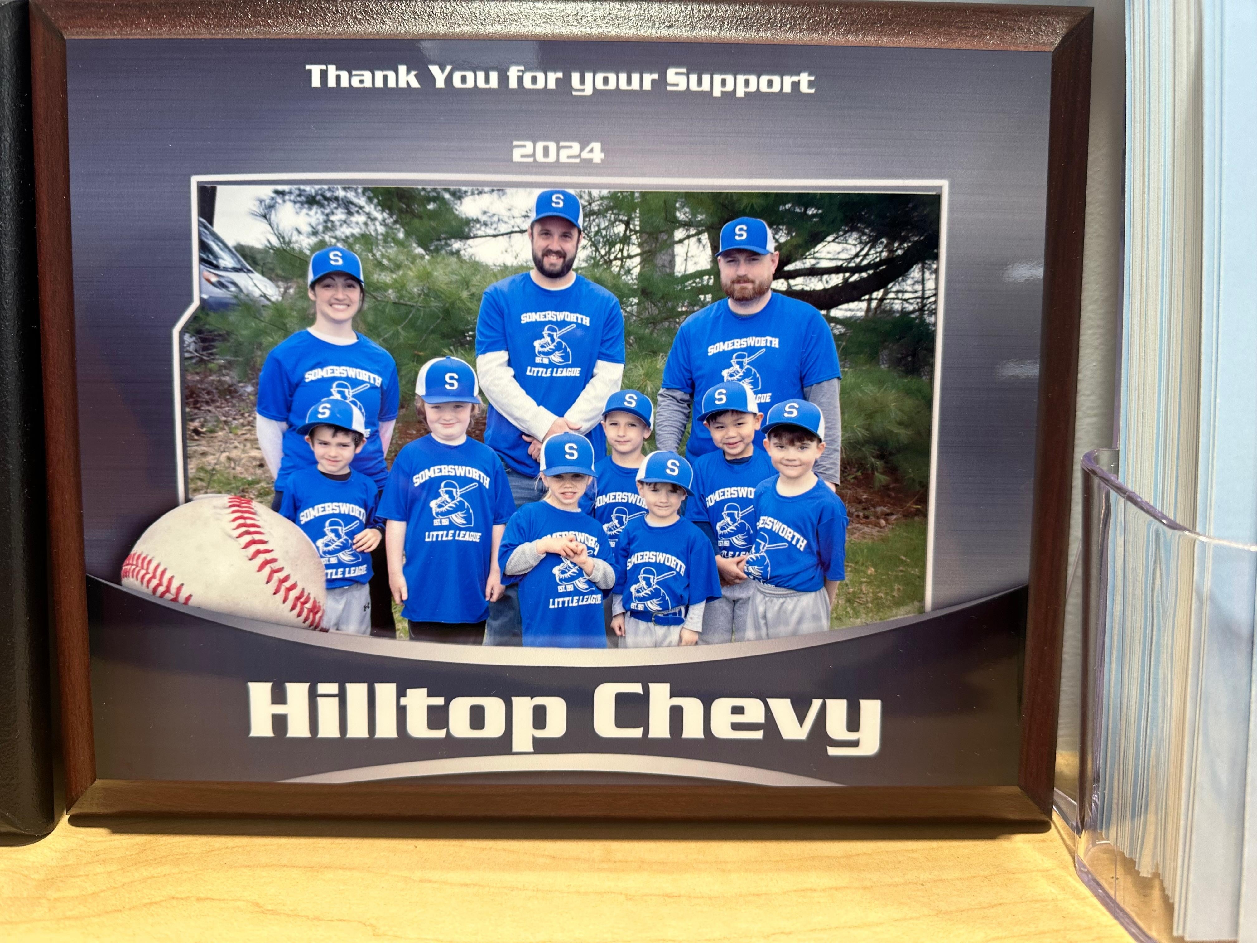 Framed photo of a youth baseball team with text Thank You for your Support, 2024, and Hilltop Chevy Team in blue uniforms with caps. Large baseball graphic on the left.