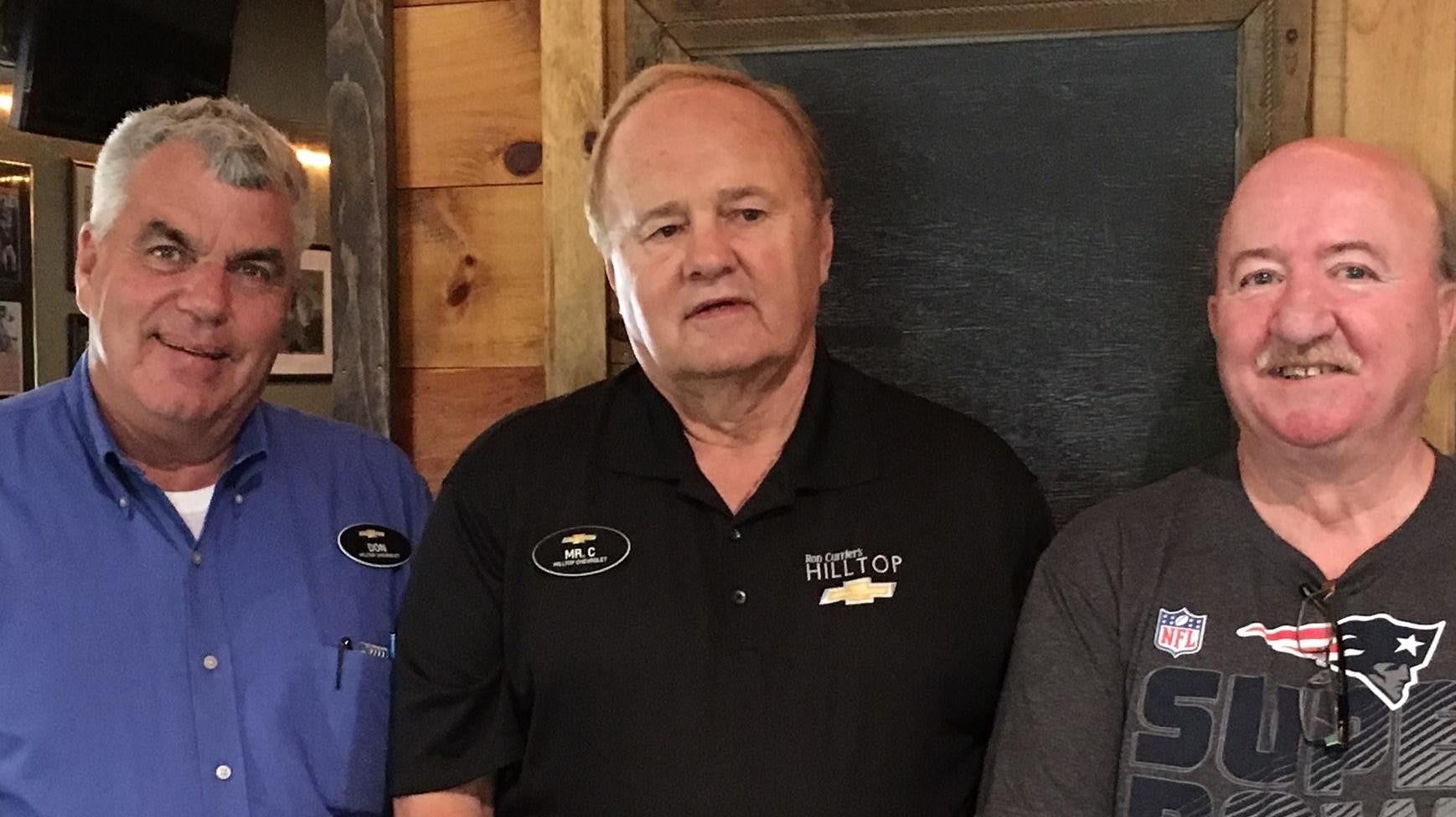 Three people standing side by side, each wearing different shirts with logos and name tags.