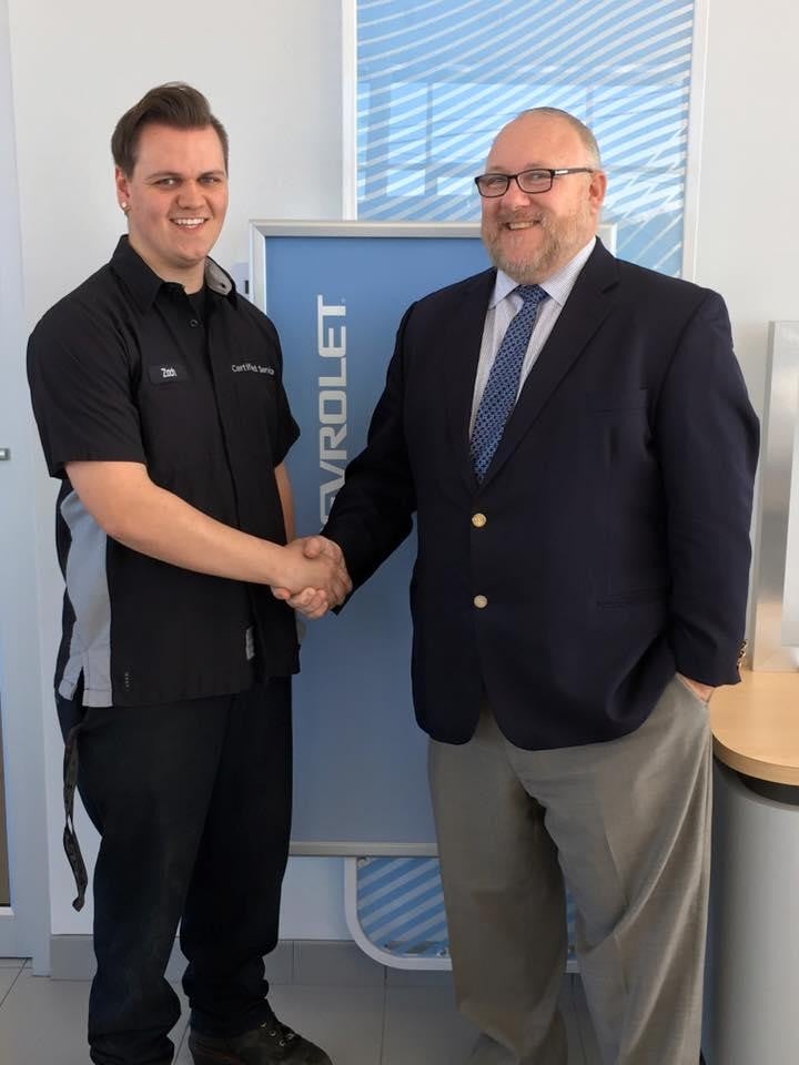 Two people shaking hands in front of a Chevrolet sign.