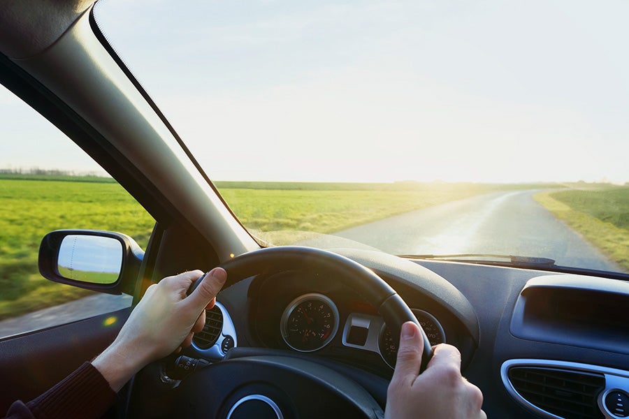 Hand on steering wheel with road ahead through windshield